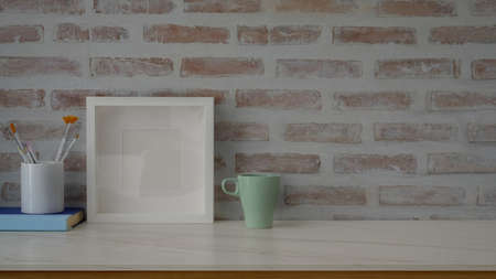 Close up view of contemporary workspace with mug, mock-up frame , painting brush and copy space on...