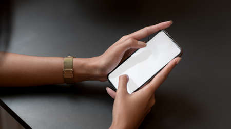 Close up view of young college girl typing on mock-up smartphone on black table while relaxing in coffee shopの写真素材