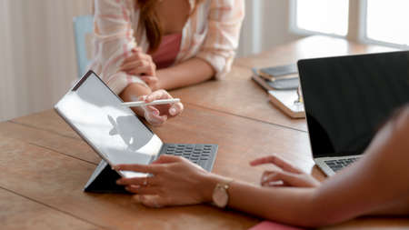 Cropped shot of two young college girl consulting on their assignment with digital tablet on wooden...