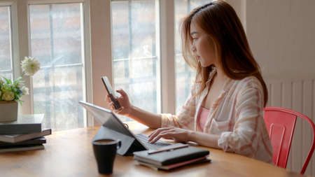 Cropped shot of young college girl working on her assignment with tablet, smartphone and stationery...