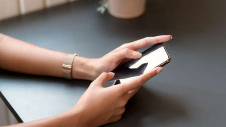 Cropped shot of young college girl typing on smartphone on black table while relaxing in coffee shop
