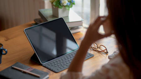 Cropped shot of young college girl calling phone while sitting at comfortable working space with digital tablet and stationery on wooden deskの写真素材