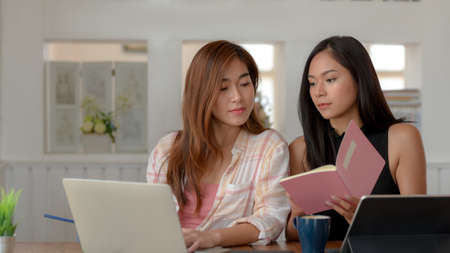 Close up view of two young college girl brainstorming on their assignment with laptops and notebook in comfortable living roomの写真素材