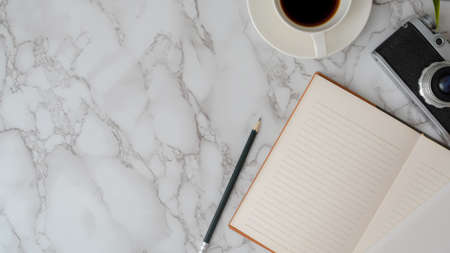 Overhead shot of modern workspace with open notebook, pencil, camera, coffee cup and copy space on marble desk   の写真素材
