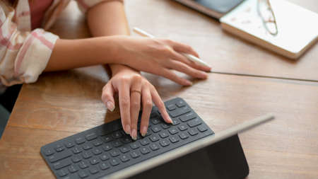 Close up view of young college girl typing on digital tablet on wooden table with glasses and...