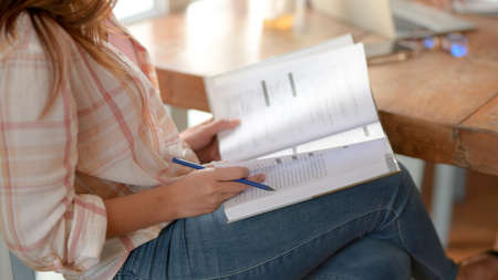 Side view of young college girl sitting in  coffee shop while reading book on her lap  to prepare...