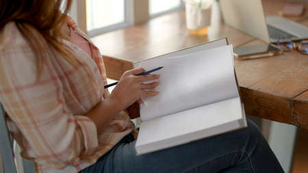 Close up view of young college girl sitting in  coffee shop while reading book on her lap  to...