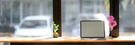 Cropped shot of working space with blank screen tablet and flower vases on wooden counter bar in coffee shopの写真素材