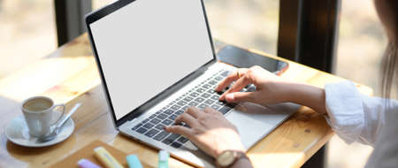 Close up view of young female university student typing on laptop on wooden table in coffee shop