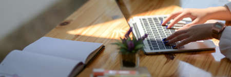 Cropped shot of  young woman university student typing on laptop with notebook and stationery on...