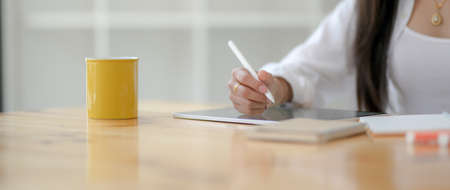 Cropped shot of young female university student writing on digital tablet with stylus pen on wooden...