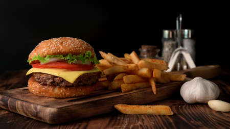 Close up view of Fresh tasty beef burger and french fries on wooden tray with seasoning and garlic on rustic tableの写真素材