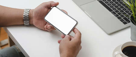 Cropped shot of male entrepreneur holding horizontal mock-up smartphone while working with office...