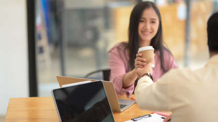 Close up view of male University student  giving cup of hot coffee to his friend while reading together in coffee shopの写真素材