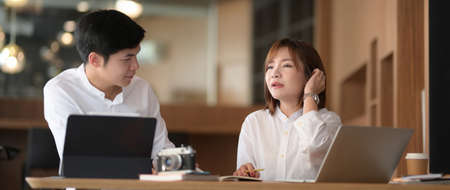 Close up view of two businesspeople discussing on their work with computer laptop on white desk in modern office roomの写真素材