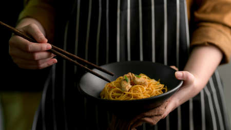 Close up view of a woman holding Schezwan Noodles or Chow Mein bowl and chopsticksの写真素材