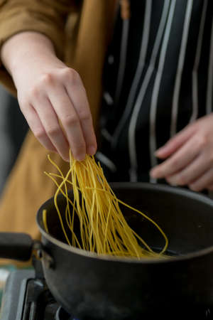 Cropped shot of young woman cooking in her kitchen room and preparing ingredients for noodle menu