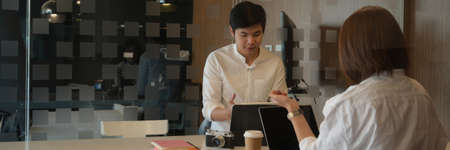 View through glass window of two photographer concentrating on their project with laptop and camera...