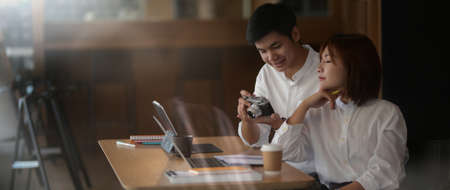 View through glass window of two businesspeople preparing their project with digital device and...