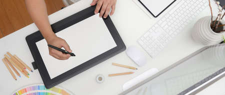 Overhead shot of designer working on  mock-up tablet, computer device and designer supplies on white...