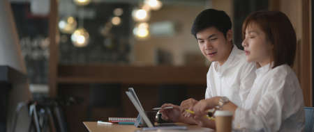 Side view of two businesspeople sitting in co-working space while consulting on their project with...