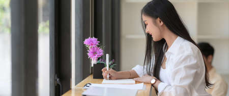 Side view of young female college student take short note while reading text to prepare for her final examの写真素材