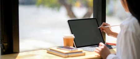 Cropped shot of young female college student focusing on her assignment with tablet, coffee cup and...