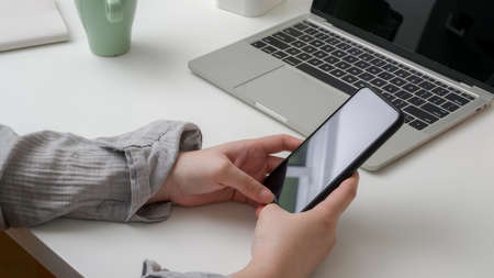 Cropped shot of female college student using smartphone to relax from doing homework on white table