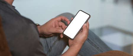 Cropped shot of a man sitting at modern living room and using blank screen smartphoneの写真素材