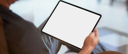 Cropped shot of a man sitting at modern living room and using blank screen digital tablet 