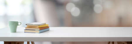 Cropped shot of simple workspace with  coffee cup, books and copy space on white table with blurred backgroundの写真素材