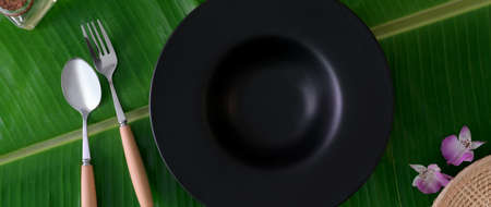 Top view of ceramic plate with spoon and folk on banana leaf background, eco-friendly restaurant...