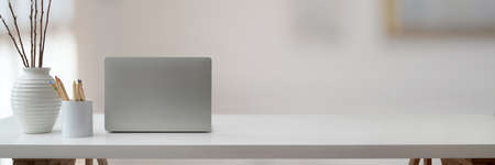 Cropped shot of simple workspace with laptop, stationery, ceramic vase and copy space on white table in living room  の写真素材