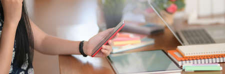 Side view of female college student using smartphone to relax from doing homework with digital...