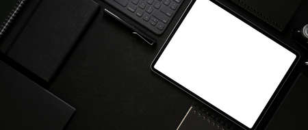 Top view of dark workspace with mock-up tablet, wireless device, office supplies and copy space on...
