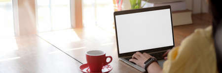 Cropped shot of young female college student typing on blank screen laptop on wooden table