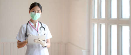 Close up view of happy female doctor writing patient chart on digital tablet in blurred examination room backgroundの写真素材