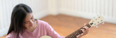 Cropped shot of young female music college student practicing guitar while sitting in music practice...