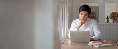 Cropped shot of young male university student focusing on his assignment with laptop while sitting in libraryの写真素材