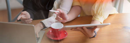 Cropped shot of two college girl consulting on their assignment with laptop, tablet and coffee cup on wooden tableの写真素材