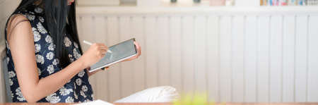 Side view of young female university student writing on digital tablet while sitting in modern living roomの写真素材