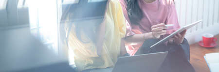View through glass window of two music student girls using digital devices to consult their project