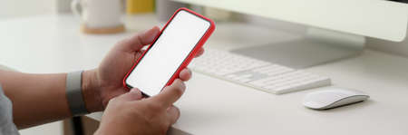 Cropped shot of a man using mock-up smartphone while relaxing in minimal office desk 