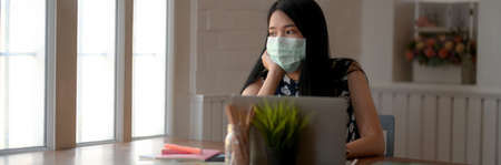 Cropped shot of young female wearing mask to prevent her self from Coronavirus and air pollution while doing homework in libraryの写真素材
