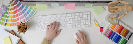 Overhead shot of female designer typing on computer keyboard on white table with designer suppliesの写真素材