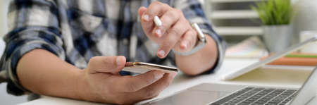 Cropped shot of male entrepreneur using smartphone while working with digital tablet and laptop on...