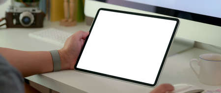 Cropped shot of a man holding blank screen tablet on white table with computer device and coffee cup