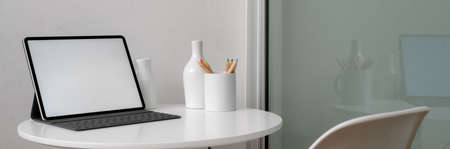 Cropped shot of portable workspace with mock-up tablet and ceramic decorations on white circle table...