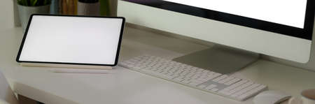 Cropped shot of office desk with blank screen computer devices on white table in comfortable office...