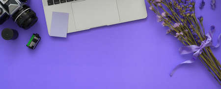 Top view of feminine photographer workspace with laptop, camera, flowers and copy space on purple...